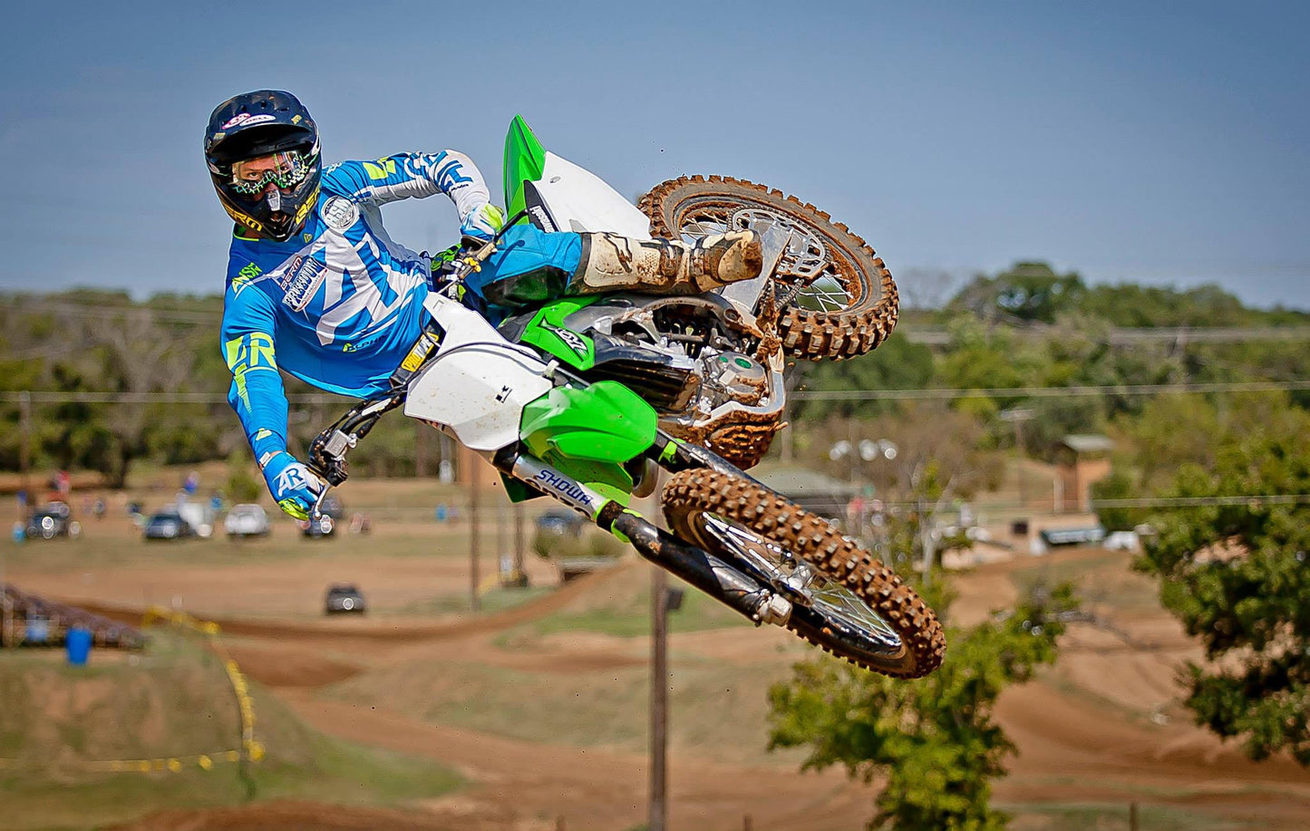 A Kawasaki dirt bike rider jumping his dirtbike with green Shock Sox on it.