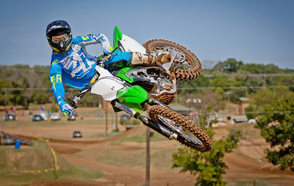 A Kawasaki dirt bike rider jumping his dirtbike with green Shock Sox on it.