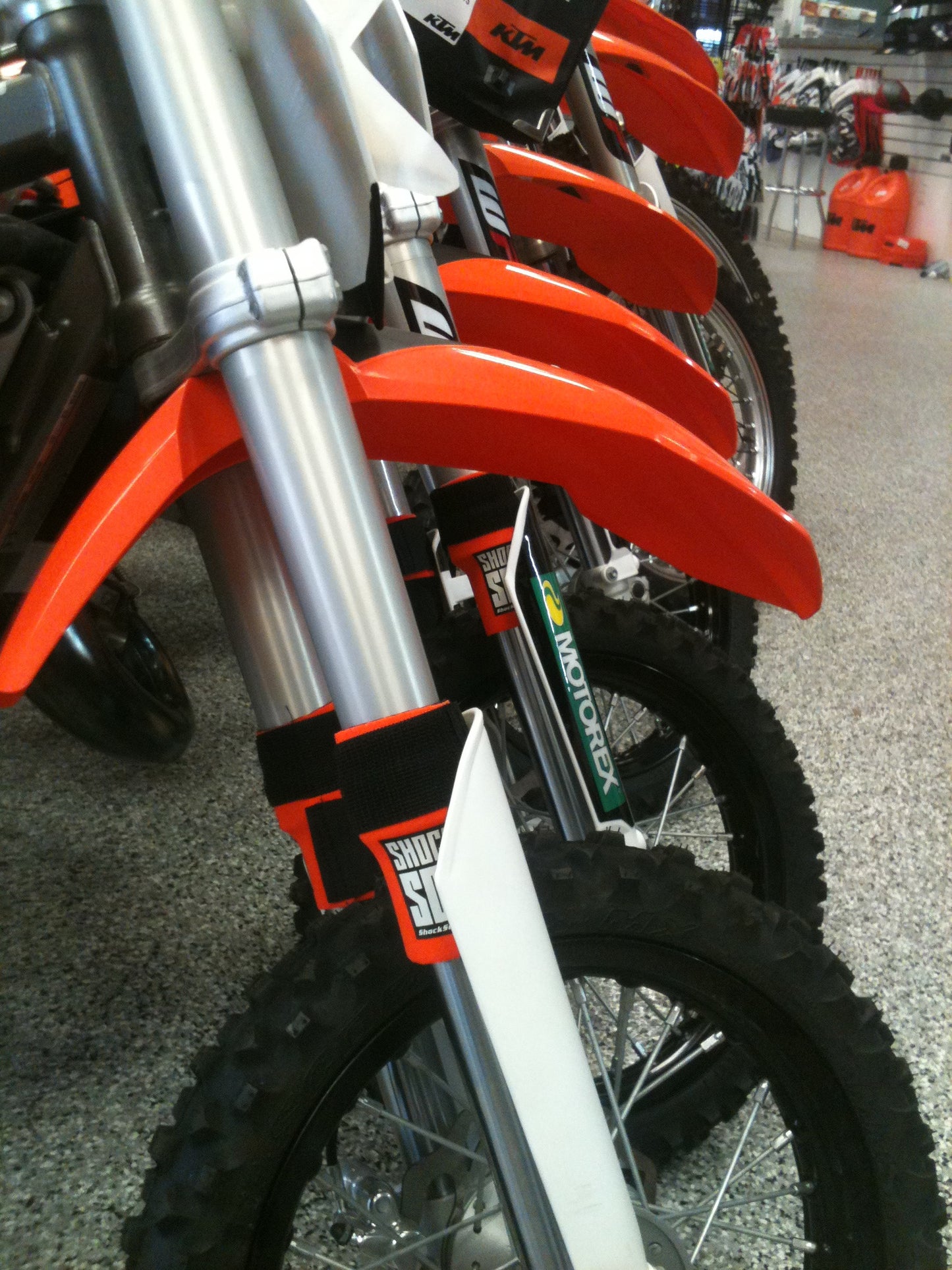 A picture of multiple KTM dirt bikes with orange Shock Sox on them.